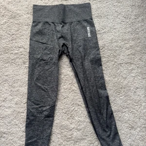 Mörkgrå träningstights från Gymshark - Säljer ett par mörkgrå träningstights från Gymshark med hög midja och diskret logga på benet. Tightsen är stretchiga och sitter tight, perfekta för gymmet eller löpning.