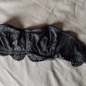 NY Svart spets bandeau 70C från Victoria's Secret - Supersnygg svart bandeau topp från Victoria's Secret i spets med blommigt mönster. Axelbandslös modell med fina volangdetaljer längs kanten. Perfekt att styla under en öppen skjorta eller kavaj för en trendig look. Oanvänd med tags kvar.