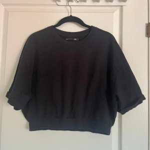 Svart croppad tröja från lager 157 - Svart croppad tröja från lager 157 med rund halsringning och uppvikta ärmar. Perfekt för en avslappnad och trendig stil. Mjuk och bekväm, passar till många olika outfits.