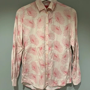 Ljusrosa skjorta med mönster från Whyred - Snygg skjorta i ljusrosa med mönster i rosa toner. Skjortan har klassisk krage, knäppning framtill och långa ärmar. Perfekt för dig som gillar en feminin och lekfull stil. Väldigt skönt material. 