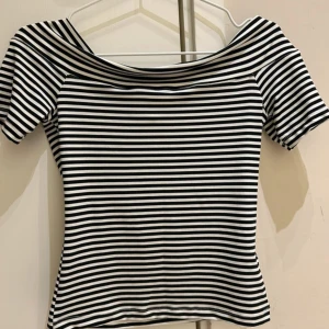 Svartvit randig offshoulder topp - Trendig topp med svarta och vita ränder och offshoulder-design. Kortärmad och figurnära passform, perfekt för en stilren och modern look. Ny utan prislapp 