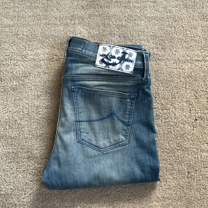 Jacob Cohën Jeans - Tja! Söljer nu dessa Jacob Cohën jeans! De är ljusblåa och har många fina detaljer (se bild). Längst ner så är den sydd ihop för att den var för lång, men det ser ut som vanligt, och det märks inte. Utöver det så är skicket 10/10, inga defekter alls! Storleken är 26, så jag skulle säga att den passar om du är 155 cm - 165 cm, och ganska smal. Perfekt för fina sommarmiddagar🥂! Tveka inte med frågor!🤝