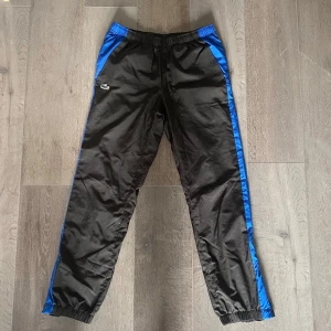 Lacoste sport byxor  - Svarta träningsbyxor från Lacoste Sport med blå linje på sidan. Använda ett fåtal gånger men i perfekt skick. Hör av er vid frågor ☺️