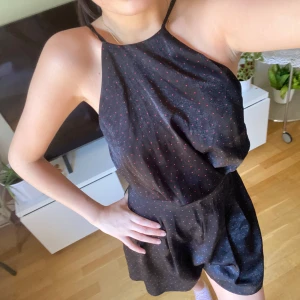 Svart short klänning med röda prickar - Säljer en svart kort klänning med tunna axelband och små röda prickar. Klänningen har en lös passform upptill och markerad midja, samt är ärmlös. Perfekt för varma dagar!