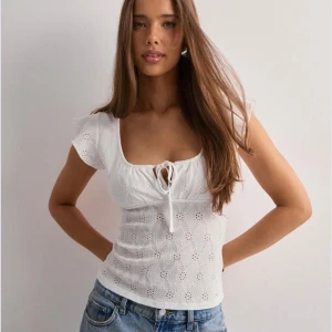 Vit broderad topp med knytning - Söt vit topp med broderade hålmönster, korta volangärmar och knytning framtill. Slutsåld topp från Nelly i storlek xs 