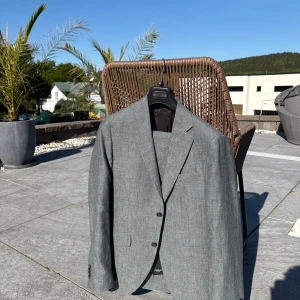 Cavaliere Cougar grön linnekostym, nypris 7600kr - Snygg grön linnekostym från Cavaliere Cougar med klassisk kavaj och matchande byxor. Kavajen har två framfickor med lock, smala slag och knäppning framtill. Byxorna har pressveck och bakficka med knapp. Perfekt för formella tillfällen. PRISET KAN DISKUTERAS