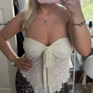 Vit spets tubtopp med knyt -  en söt vit tubtopp i spets med knyt framtill. Toppen är axelbandslös och har en romantisk känsla med volangkant nertill. Perfekt för sommardagar eller festival.