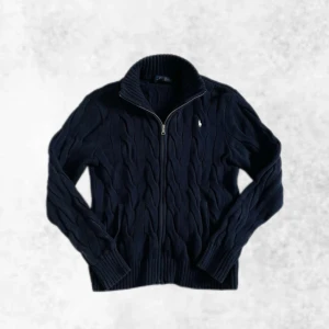Kabelstickad full zip från Ralph Lauren - Säljer denna sjukt snygga kabelstickade full zipen från Ralph Lauren med ett klassiskt kabelstickat mönster. Tröjan har en liten vit broderad logga på bröstet och ribbade muddar. Perfekt för kyliga dagar! Den är i perfekt skick utan några defekter eller likande. Storlek L men sitter som M. Vid några frågor eller funderingar är det bara att höra av sig.
