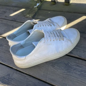 Vita sneakers från Axel Arigato - Säljer ett par stilrena vita sneakers från Axel Arigato. Skorna har en klassisk design med snörning och en bekväm sula. Perfekta för en avslappnad och trendig look.
