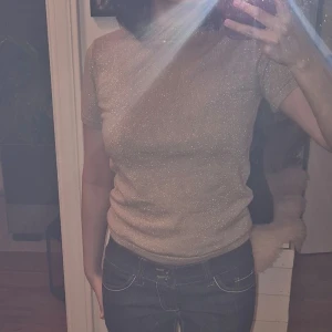 Glittrig topp - Säljer en glittrig beige topp med korta ärmar. Perfekt för en kväll ute eller en festlig tillställning. Toppen har en tight passform och ger en elegant look.