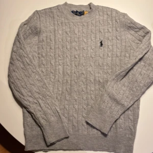 Ralph Lauren långarmad tröja stickad - Säljer en stilren grå stickad tröja från Ralph Lauren med kabelstickat mönster. Tröjan har långa ärmar och en rund halsringning. Perfekt för kyligare dagar! Helt ny endast testad på men var för liten. Skulle säga att den är för längden 170-175 så S. Hör av er vid intresse🌟