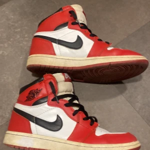Nike Air Jordans i rött och vitt - Säljer ett par klassiska Nike Air Jordans i rött, vitt och svart. Skorna har en hög design med snörning och den ikoniska Nike-loggan på sidan. Perfekta för sneakerheads som älskar retrostil.