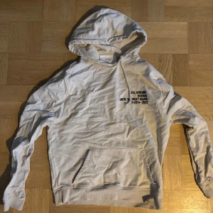 Beige hoodie från Axel Arigato - Säljer en tidlös beige hoodie från Axel Arigato med tryck på bröstet. Hoodien har en klassisk design med känguruficka och justerbar huva. Ett litet hål vid kängurufickan på höger sidan som syns på bild 3!