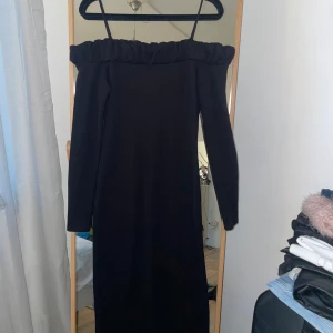 Svart offshoulder klänning från H&M - Snygg svart offshoulder klänning från H&M med ribbad struktur och slits. Perfekt för en stilren look. Klänningen har långa ärmar och en åtsittande passform som framhäver figuren.