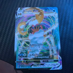 Kingler VMAX Pokémonkort - Säljer ett Kingler VMAX Pokémonkort med 330 HP. Kortet har en färgglad design och inkluderar attacker som Bubbles Galore och G-Max Pincer. Perfekt för samlare eller spelare som vill förstärka sin kortlek. Kortet har en holografisk yta som ger det en extra glans.