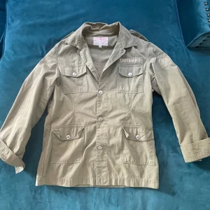 Field jacka - Snygg grön/beige field jacka med knappar och flera fickor. Perfekt för en avslappnad stil. Jackan har en klassisk krage och långa ärmar. Skick 10/10✅ Skriv vid frågor eller funderingar i DM🍾