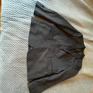 Svart kavaj från C - Snygg svart kavaj från märket C. Kavajen har en klassisk design med två knappar framtill och fickor på sidorna. Perfekt för en stilren look.