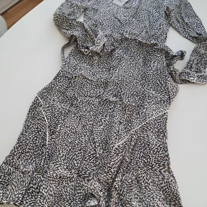 Svartvit klänning från Part Two - Snygg svartvit klänning från Part Two med ett unikt mönster. Klänningen har långa ärmar och en elegant krage. Tillverkad i 100% viskos, vilket ger ett mjukt och bekvämt fall. Perfekt för en stilren look. Klänningen är helt ny med prislappen kvar!