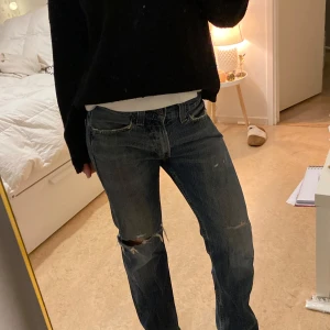 Blå jeans från Levi's - Säljer ett par klassiska blå Levi's jeans med slitna detaljer och hål vid knäna. De har en rak passform och är perfekta för en avslappnad stil.