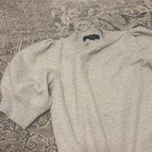 Beige tröja från Vero Moda - Säljer en stilren beige tröja från Vero Moda. Tröjan har korta ärmar med puffdetaljer och ribbade kanter vid ärmslut och nederkant. Perfekt för en avslappnad look.