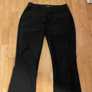 Svarta kostymbyxor från BikBok - Snygga svarta lågmidjade kostymbyxor från BikBok med en klassisk design. Byxorna har en rak passform med slits nertill och är perfekta för en stilren look. 