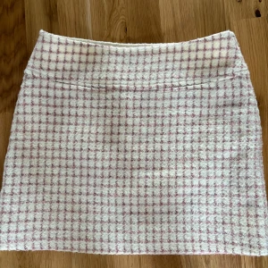 Rutig kjol från & Other Stories - Säljer en stilren rutig kjol från & Other Stories i en mjuk rosa och vit färgkombination. Kjolen har en klassisk passform och är perfekt för en chic look. Tillverkad i ett fluffigt material som ger en unik textur.