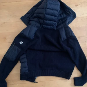 Svart jacka med huva - Cardigan blå jacka från Moncler. Den har en ficka med dragkedja på ärmen och Moncler-loggan. Shippar bara. Size L fast är sitter tight, rekommenderar för någon som är size M. Nyss skick har andvänt den lite.