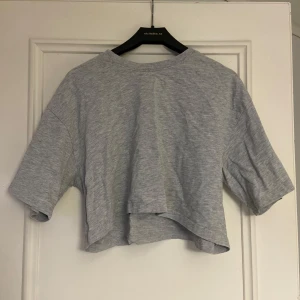 Grå croppad t-shirt från Gina Tricot - Säljer en grå croppad t-shirt från Gina Tricot. Den har en avslappnad passform med korta ärmar och är perfekt för en casual look. Gjord i mjukt material för extra komfort.