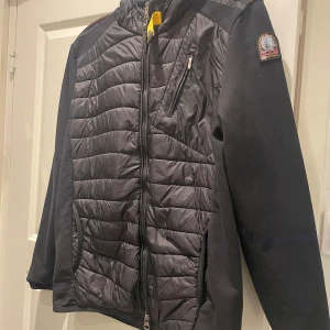 Svart jacka från Parajumpers - Säljer en svart jacka från Parajumpers med quiltad design och dragkedja. Jackan har en bröstficka med dragkedja och en huva. Perfekt nu till våren.