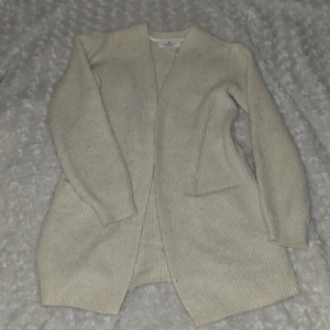 Beige ribbad kofta från H&M - Säljer en stilren beige ribbad kofta från H&M. Perfekt för lager-på-lager och har en öppen design utan knappar. Den är långärmad och gjord i ett mjukt material som passar bra för kyligare dagar.