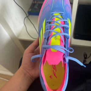 Adidas blå/gula fotbollsskor X Speedflow - Säljer ett par Adidas X Speedflow fotbollsskor i en riktigt fet färgkombo: blå bas med neonrosa och gula detaljer. Skorna har snörning, platt sula med dobbar och är tillverkade i syntetmaterial för max speed på planen. Perfekta för dig som vill sticka ut på matchen! Kommer också med fotbollsko påse, extra sulor och såklart adidas paketet med den den är bara testad och inte använd