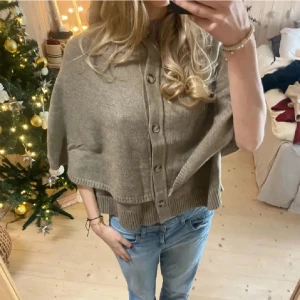 Beige stickad poncho med knappar - Supermysig beige stickad kofta med bred passform och snygga träknappar framtill.  Lapparna är bortklippta då jag tyckte de kliade. Nypris:699 (har flyttat till Spanien så den kommer behöva skickas härifrån!)