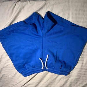 Blå shorts med snörning från Lindex - Blå mjuka shorts från Lindex med vit snörning i midjan och elastisk resår. Modellen är loose fit och passar perfekt för chill dagar. Materialet är bomull och de har en enkel, stilren look utan mönster eller extra detaljer.