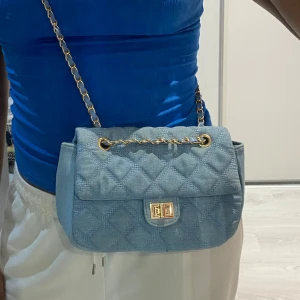 Ljusblå axelväska - En rymlig väska där du gå i mycket saker. Den har en ett innerfack även! Blå axelväska med fina gulddetaljer.