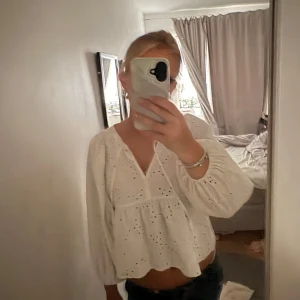 Vit blus med broderade detaljer - Säljer en söt vit blus med broderade hålmönster och v-ringning. Blusen har långa puffiga ärmar med resår vid handlederna och en lös, flowy passform. Perfekt för dig som gillar romantisk och bohemisk stil. Alldeles för liten på mig, kort i armarna. Väldigt fin! Kommer från DOBBER och kostar i nypris 700-800 kr.