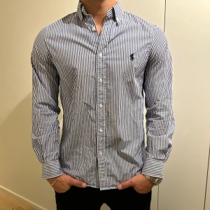 Ralph Lauren skjorta - Snygg skjorta från Ralph Lauren som är randig med blå och vit. Tröjan är helt ny endast använd en gång och har inga defekter. Nypris ca 1000kr. Hör av dig vid frågor eller funderingar