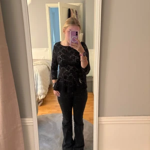 Svart spetsblus med peplum  - Supersnygg svart blus i spets från New yorker med blommigt mönster, peplum nedtill och trekvartsärm. Blusen har rund halsringning och dragkedja i ryggen.