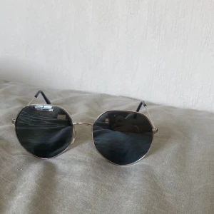 Solglasögon med silvrig båge - Snygga solglasögon med tunn silvrig metallbåge. Skalmarna är smala med svarta ändar för extra komfort. Perfekt accessoar för en cool och stilren look.