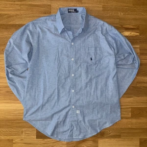 Blå skjorta från Polo Ralph Lauren XXL - Helt ny blå skjorta från Polo Ralph Lauren i 100% bomull. Skjortan har lång ärm, knappar framtill och en bröstficka med den ikoniska broderade polospelaren. Mått: längd: 70cm. Bredd: 60cm