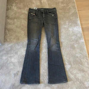 Grå bootcut jeans från Diesel - Snygga grå jeans från Diesel med bootcut passform och klassisk femficksdesign. Jeansen har slitna detaljer och en cool tvätt som ger en avslappnad vibe. Märkespatch bak i midjan och dragkedjegylf. Perfekta för dig som gillar en tidlös men trendig look. Köptes för 1800kr