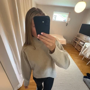 Beige stickad polotröja från H&M - Säljer en beige stickad polotröja från H&M i storlek M. Tröjan har en hög ribbad krage, långa ärmar och breda muddar vid ärmslut och nederkant. Perfekt för lager-på-lager och chill stil. Superenkel att matcha med jeans eller svarta byxor.