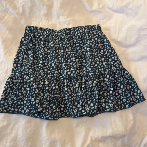 Blommig kortkjol med volang - Supersöt kortkjol i mörkblått med vita småblommor och volang nertill. Perfekt för dig som gillar en feminin och lekfull stil. Resår i midjan för skön passform.