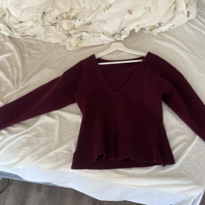 Vinröd v-ringad tröja med slits - Säljer en vinröd tröja i storlek S med v-ringad hals och långa ärmar. Tröjan har en snygg slits i sidorna och är tillverkad i mjuk polyester. Passformen är normal och materialet känns skönt mot huden. Perfekt för dig som gillar stilrena och enkla plagg.