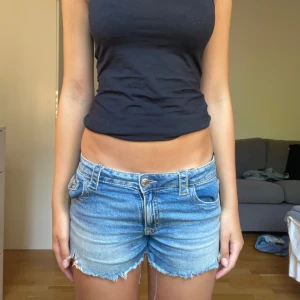 Blå lågmidjade jeansshorts - Snygga blå jeansshorts med låg midja och fransig kant. Shortsen har klassiska fickor fram och bak med lock och knappdetaljer. Perfekt tvättad denim-look som ger en chill vibe. Passar dig som gillar en avslappnad stil på sommaren.