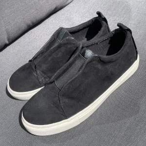 Svarta slip-on sneakers River Island - Svarta slip-on sneakers från River Island i mocka imitation med vit platt sula. Snygg broderad text 'not yours' baktill och bred resår framtill för enkel påtagning. Perfekta för en chill och stilren look. Använda fåtal gånger, bra skick! Storlek 4 som ska motsvara 36