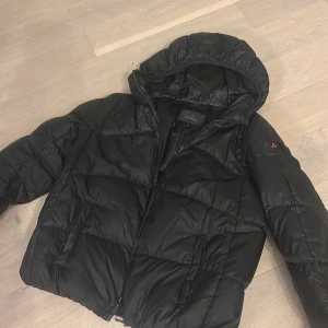Svart pufferjacka från Peuterey - Svart pufferjacka från Peuterey med huva och dragkedja. (Nypris=4700kr).Jackan har quiltad design, två fickor framtill och diskret logga på ärmen. Perfekt för kalla dagar och riktigt skön att bära. Klassisk look som funkar till det mesta.