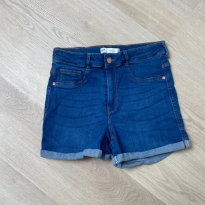Blå jeansshorts från Perfect Jeans - Snygga blå jeansshorts från Perfect Jeans, modell Molly. Klassisk femficksdesign med uppvikta ben och kontrastsömmar. Hög midja och mjukt denimtyg som sitter skönt. Perfekt för chill dagar och sommarhäng. High Waist. 