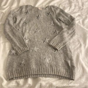 Grå stickad tröja med stjärnor H&M - Säljer en grå stickad tröja från H&M i storlek 134/140. Tröjan har långa ärmar och är dekorerad med glittriga stjärnor över hela framsidan. Perfekt för dig som gillar lite extra glitter!