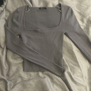 Grå ribbad långärmad topp från Gina Tricot - Säljer en grå ribbad långärmad topp från Gina Tricot i storlek S. Tröjan har fyrkantig urringning och tumm hål i ärmarna. Endast använd ett få tal gånger 