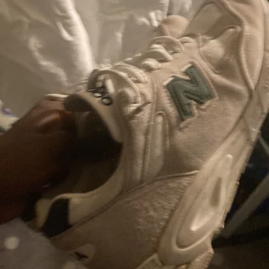 Beige New Balance 990 sneakers - Säljer ett par klassiska New Balance 990 sneakers i beige med grönt N på sidan. Skorna har en chunky siluett, meshpaneler och detaljer i mocka. USA-brodyr på hälen och vita snören. Perfekt för dig som gillar retrostil och vill ha bekväma sneakers med cool vibe.